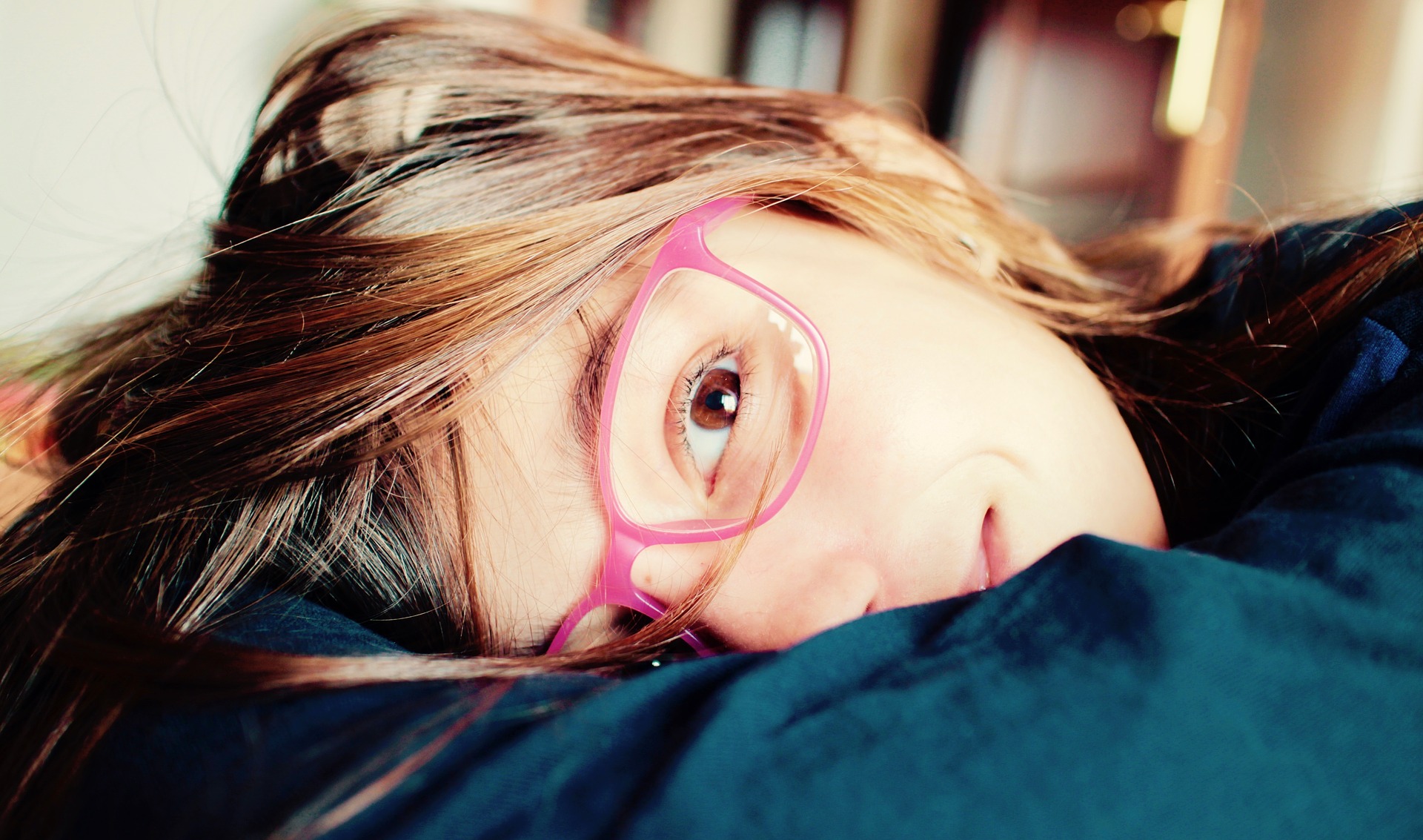 Fillette à lunettes roses allongée, le regard fatigué