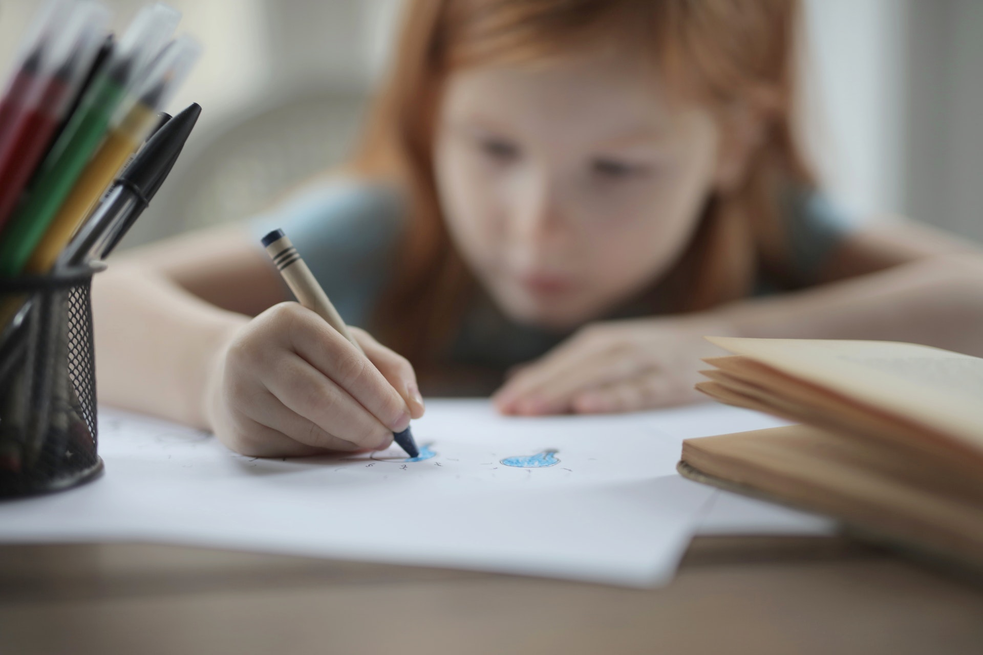 Fillette qui écrit sur une feuille, crayons de couleur à côté
