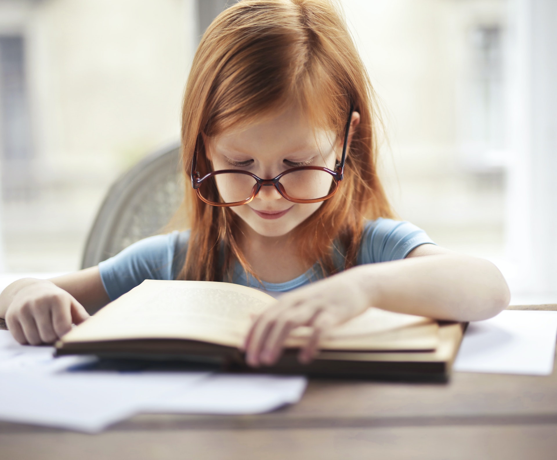 Fillette avec des lunettes, concentrée sur un livre ouvert à une table