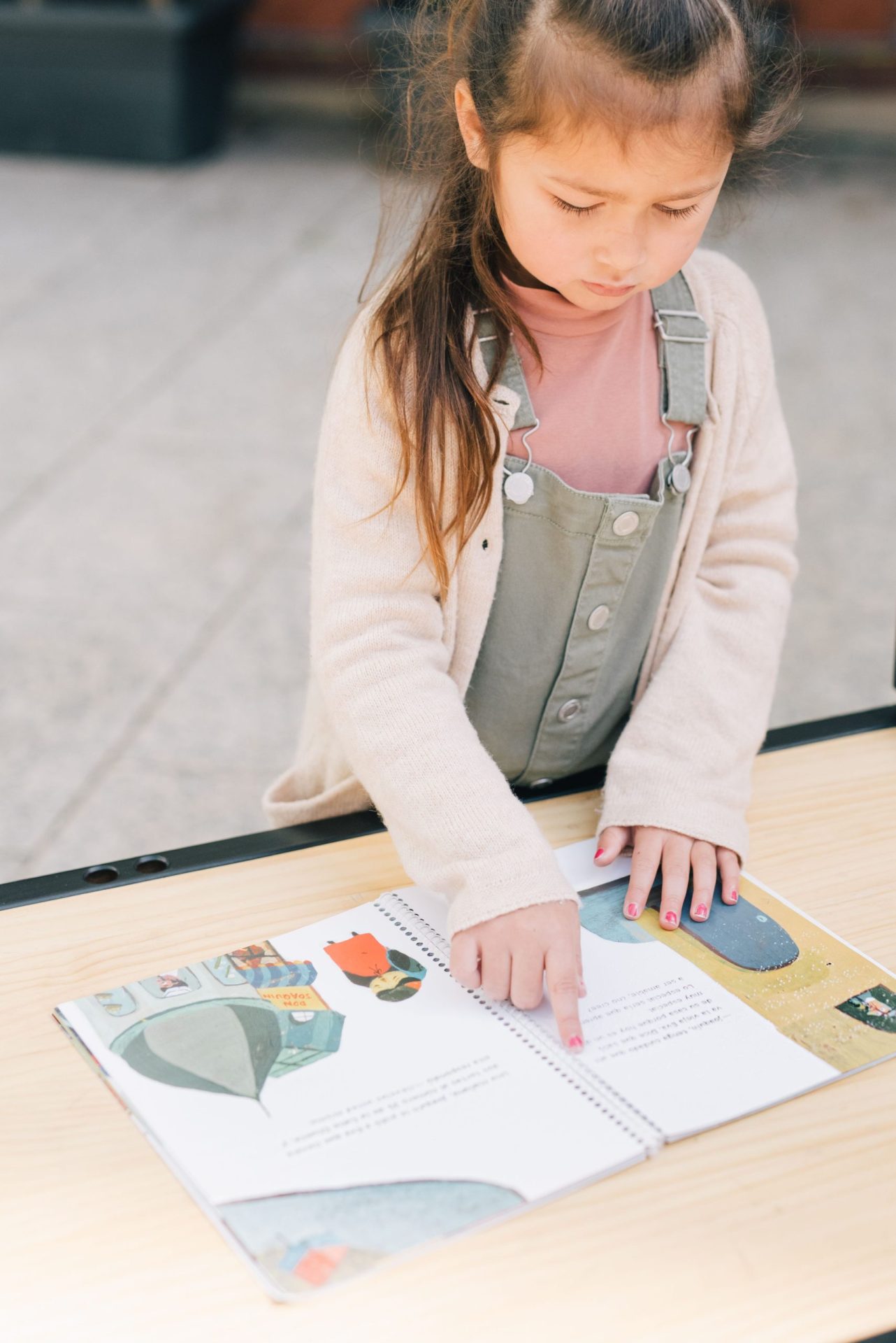Petite fille suivant du doigt les lignes d'un album posé sur une table