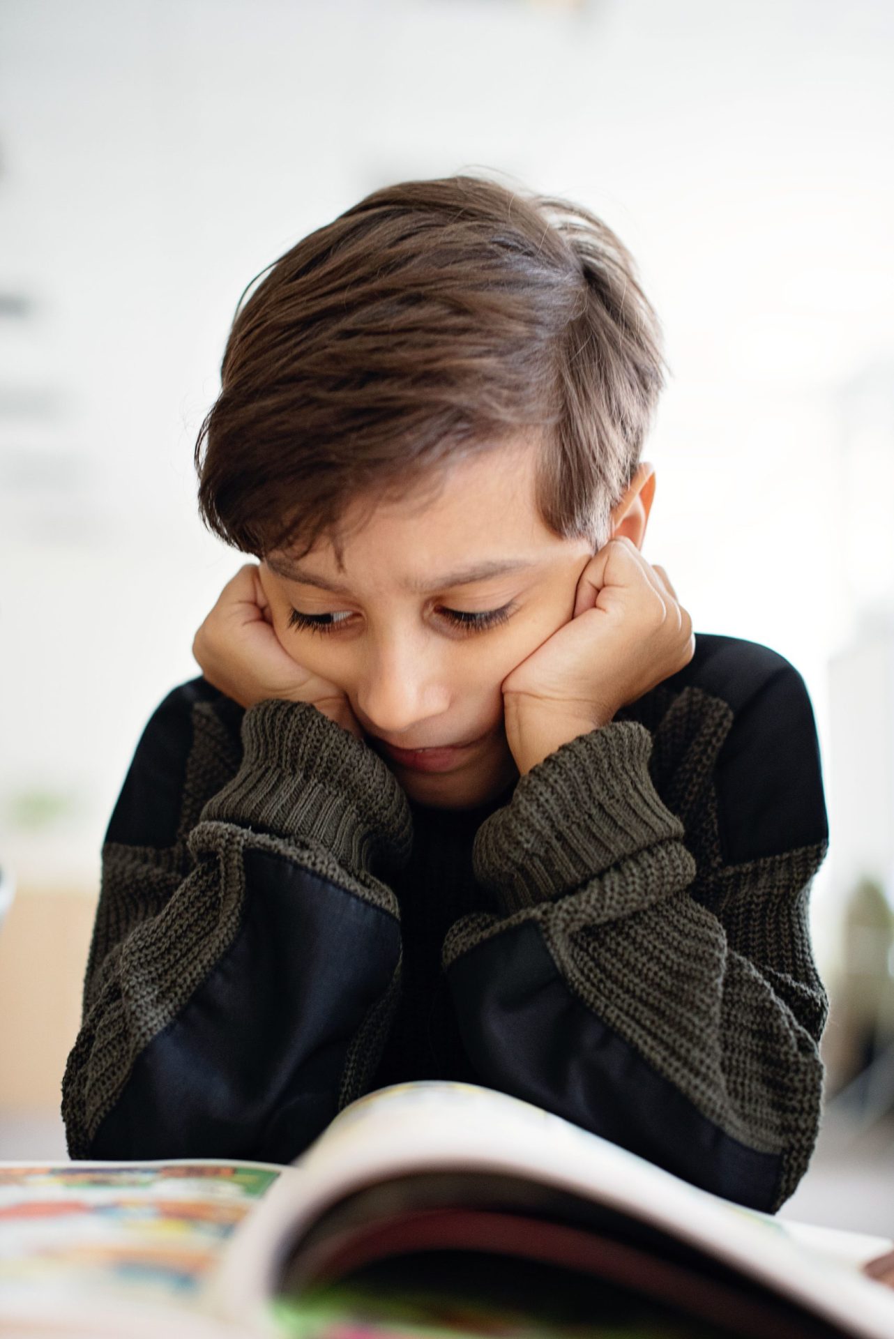 Enfant les poings contre les joues, mâchoire crispée au-dessus de son livre