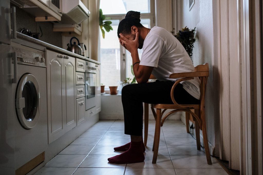 Homme assis dans sa cuisine le matin, la tête dans la main, fatigué