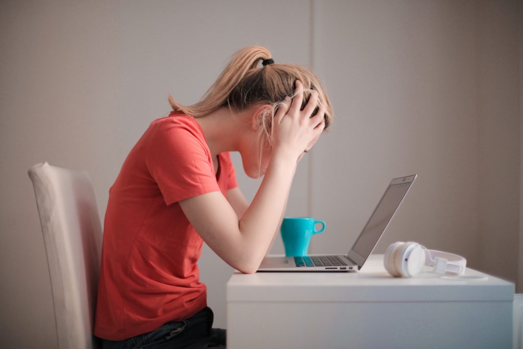 Jeune femme devant son ordinateur, les mains sur la tête, la tête lourde de fatigue