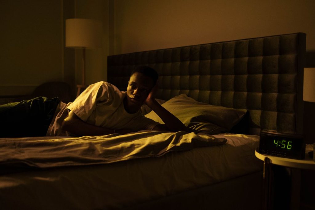 Homme réveillé dans son lit en pleine nuit, le réveil affiche 4 h 56