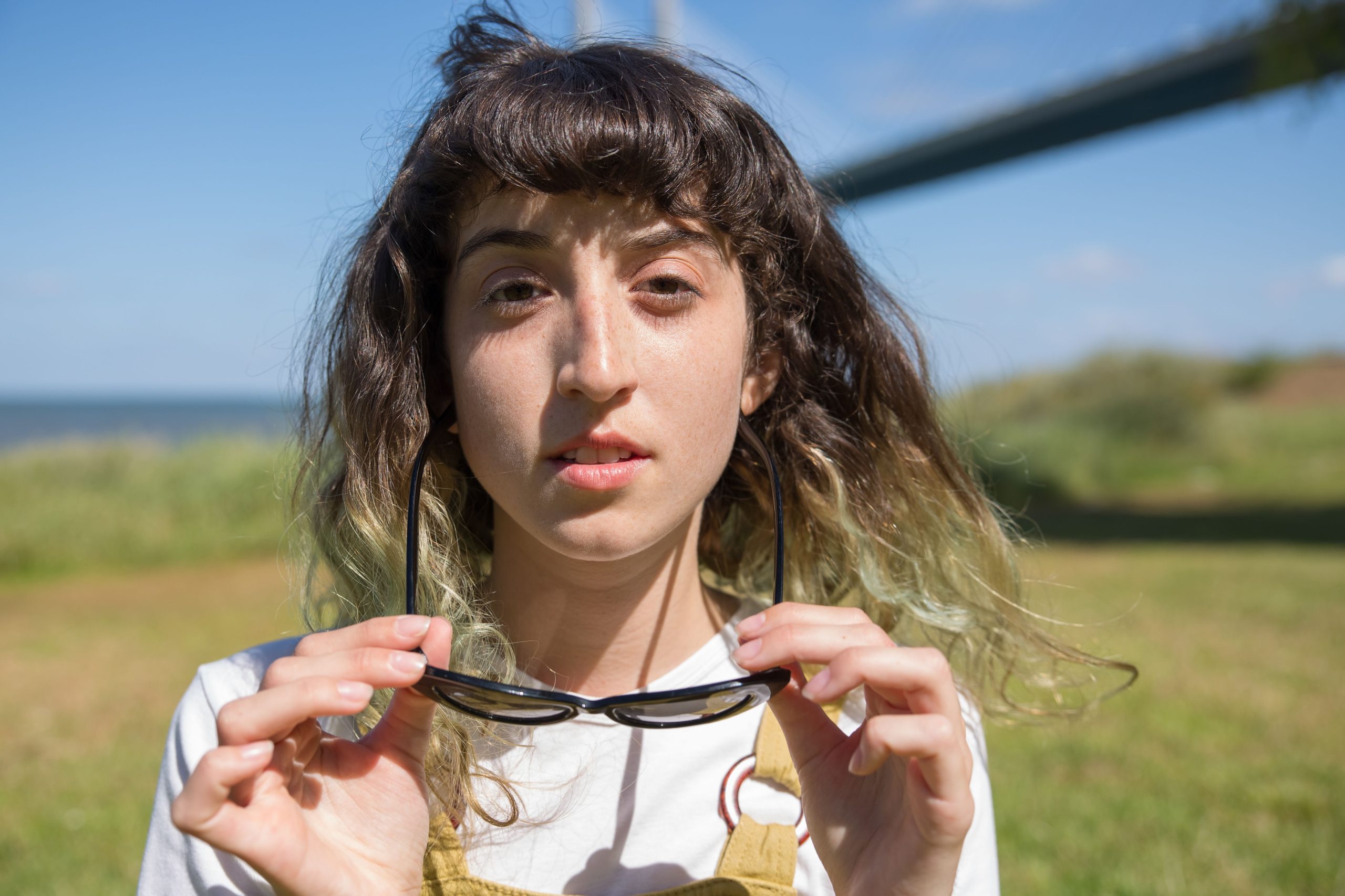 Jeune femme qui plisse les yeux au soleil, ses lunettes de soleil à la main