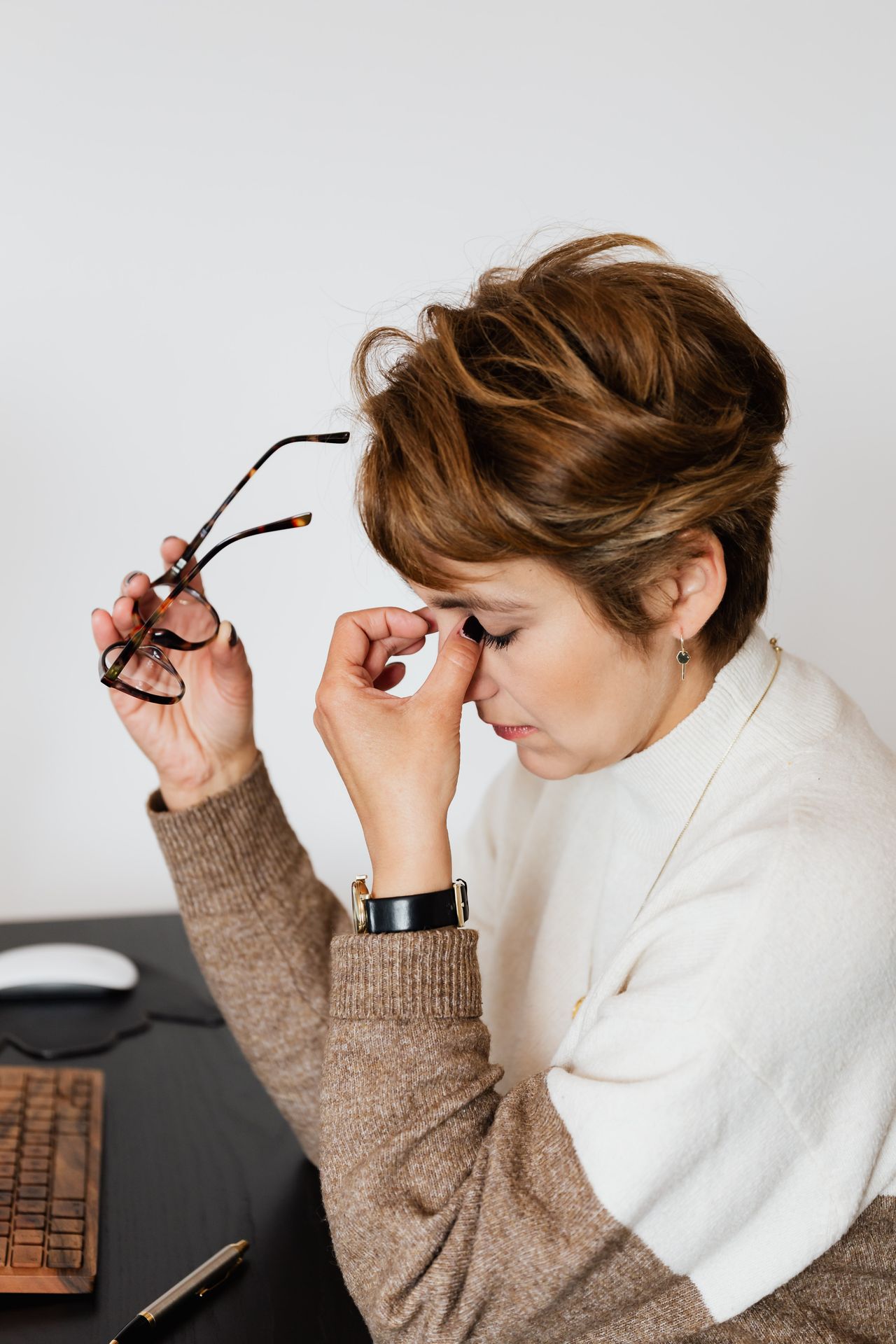 Femme épuisée à son bureau, ses lunettes à la main, qui se pince l'arête du nez