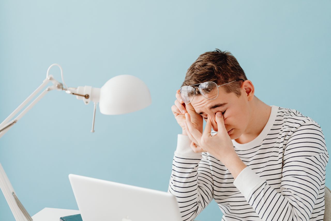 Jeune homme qui se frotte les yeux devant son ordinateur portable