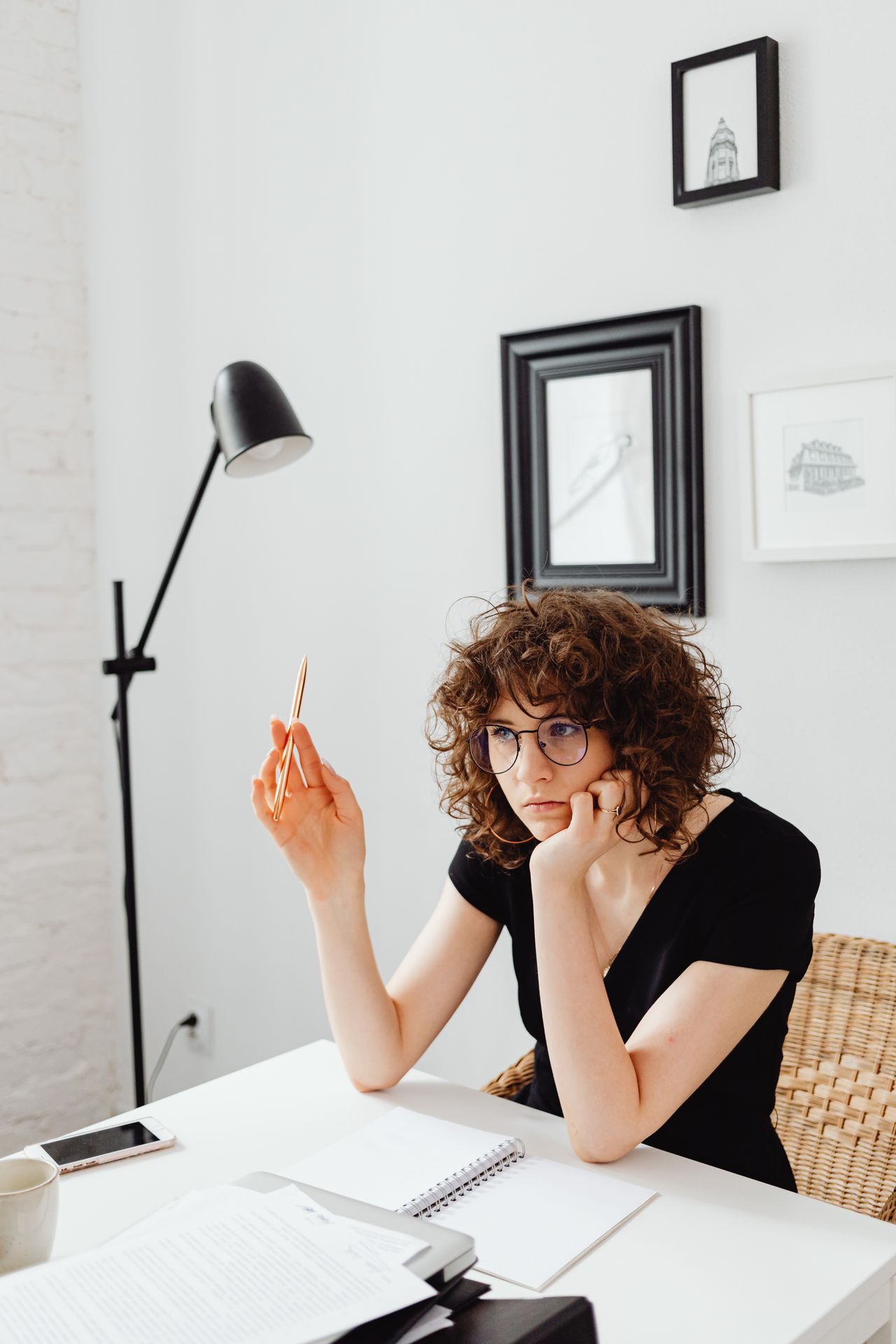 Femme aux cheveux bouclés assise à son bureau, un stylo à la main, l'air absent