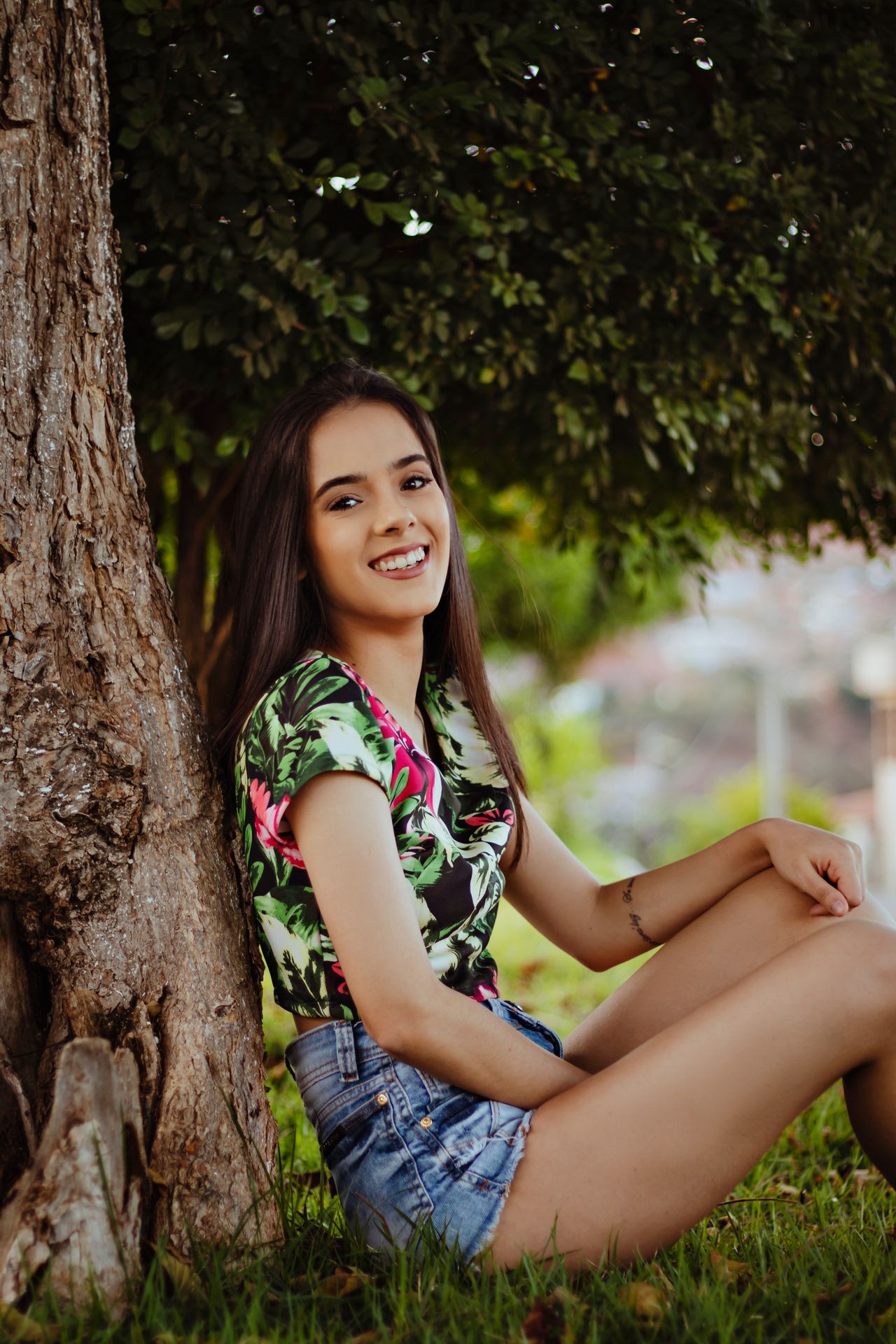 Jeune femme souriante, assise au pied d'un arbre dans un parc