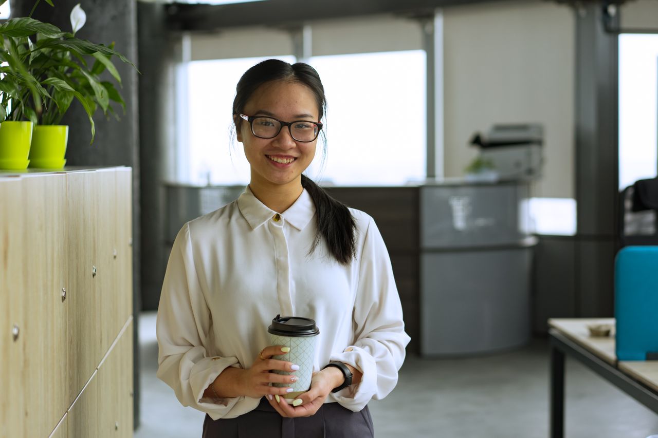 Femme souriante, un café à la main, dans un bureau lumineux