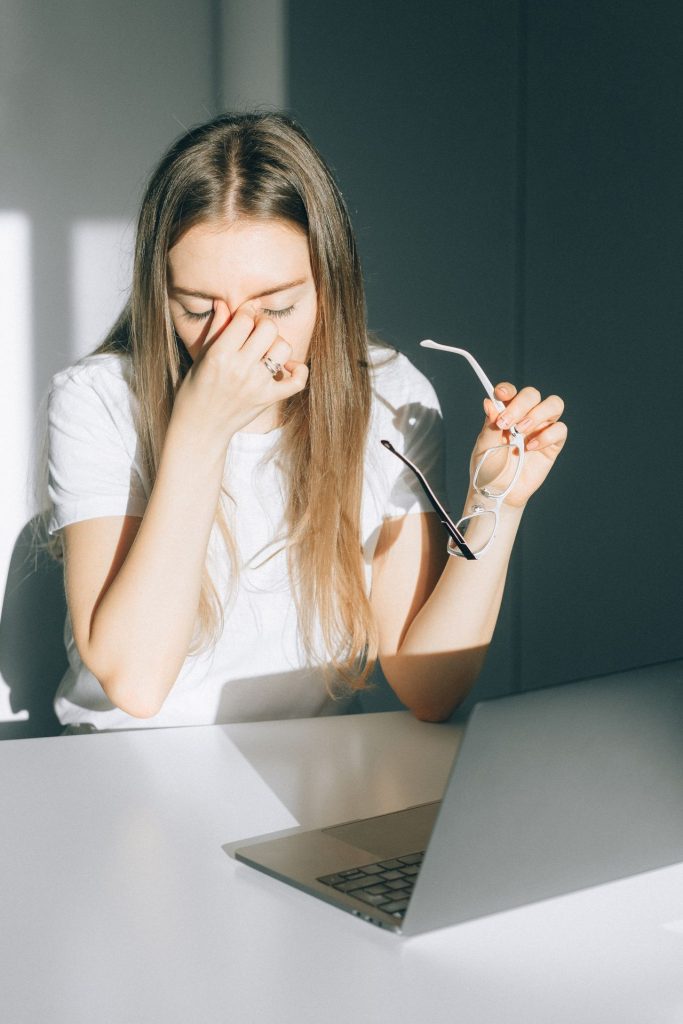 Femme qui tient ses lunettes devant l'écran