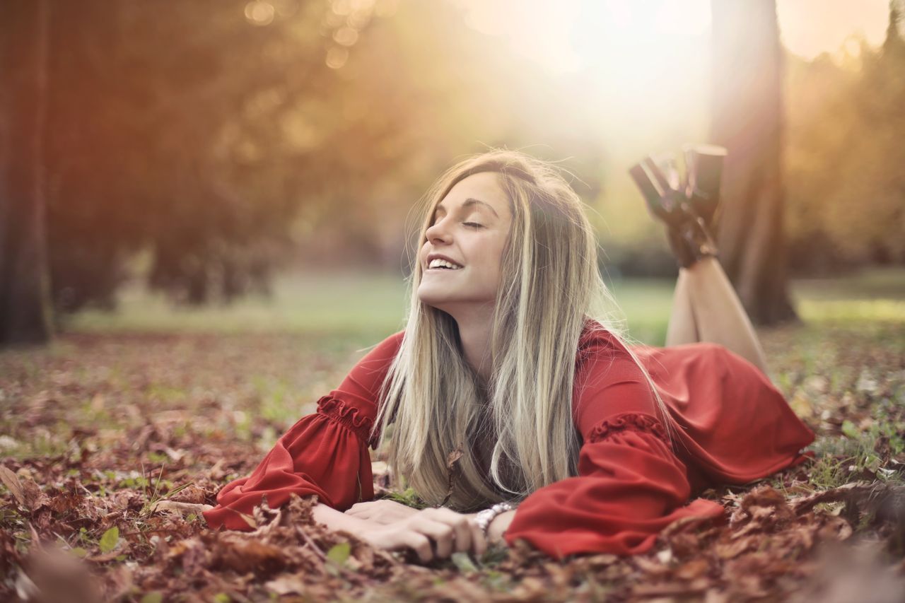 Femme blonde souriante, allongée dans les feuilles d'automne au soleil