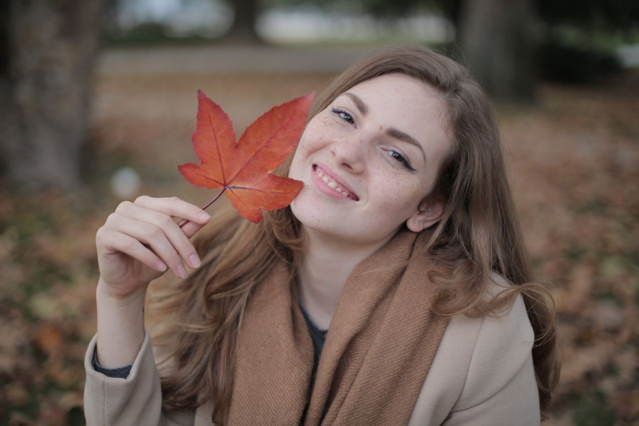 Femme souriante avec une feuille rouge, dans un parc en automne