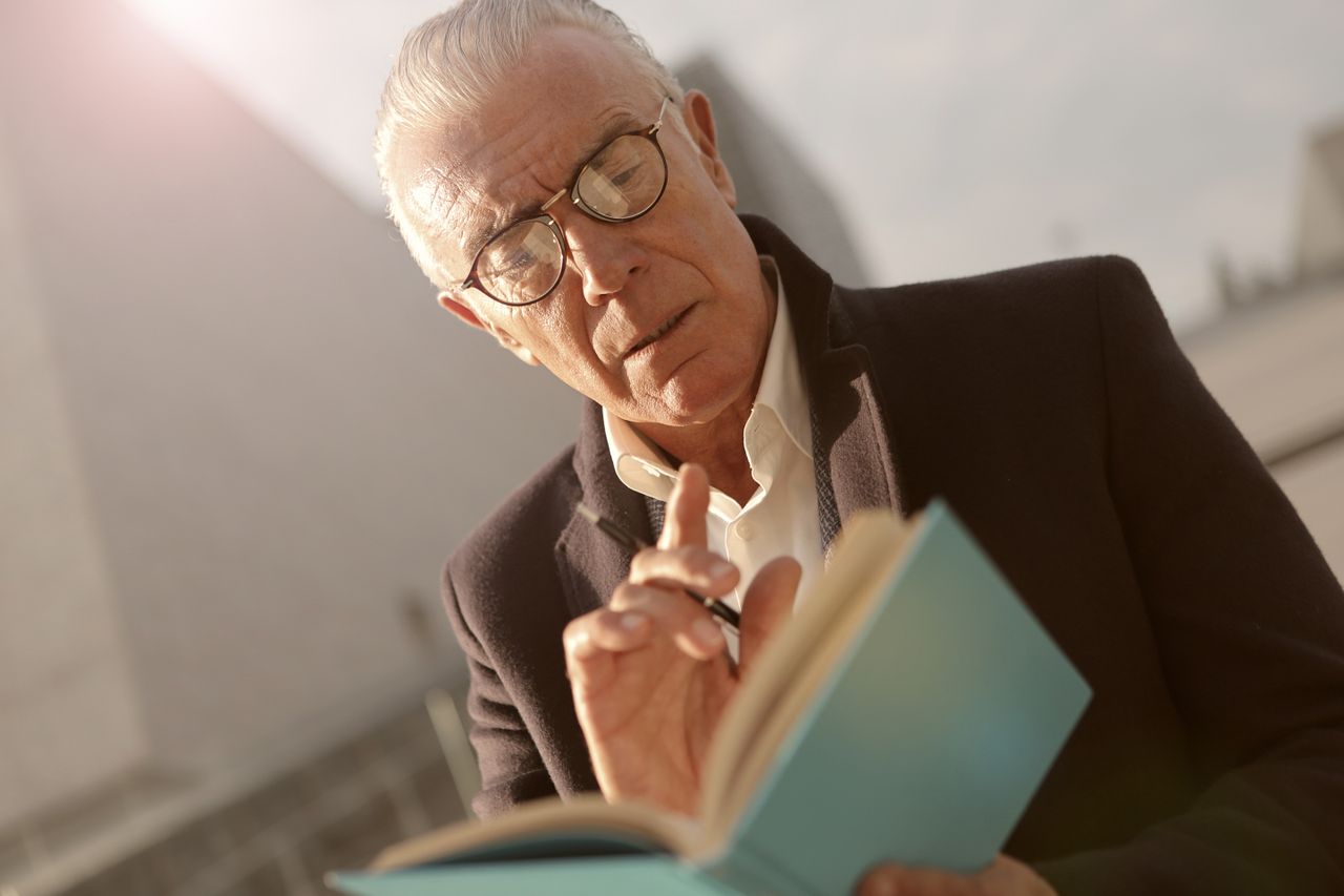 Homme âgé à lunettes qui lit un livre, le doigt levé, concentré