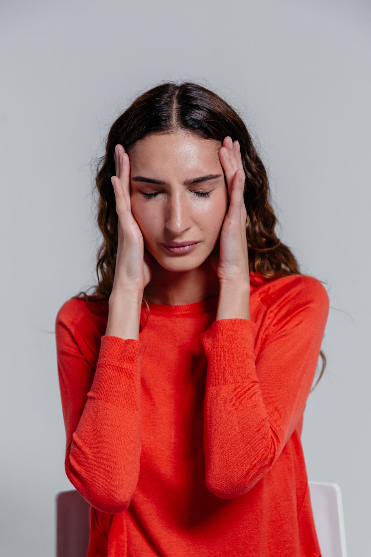 Jeune femme en pull rouge, les mains sur les tempes, les yeux fermés