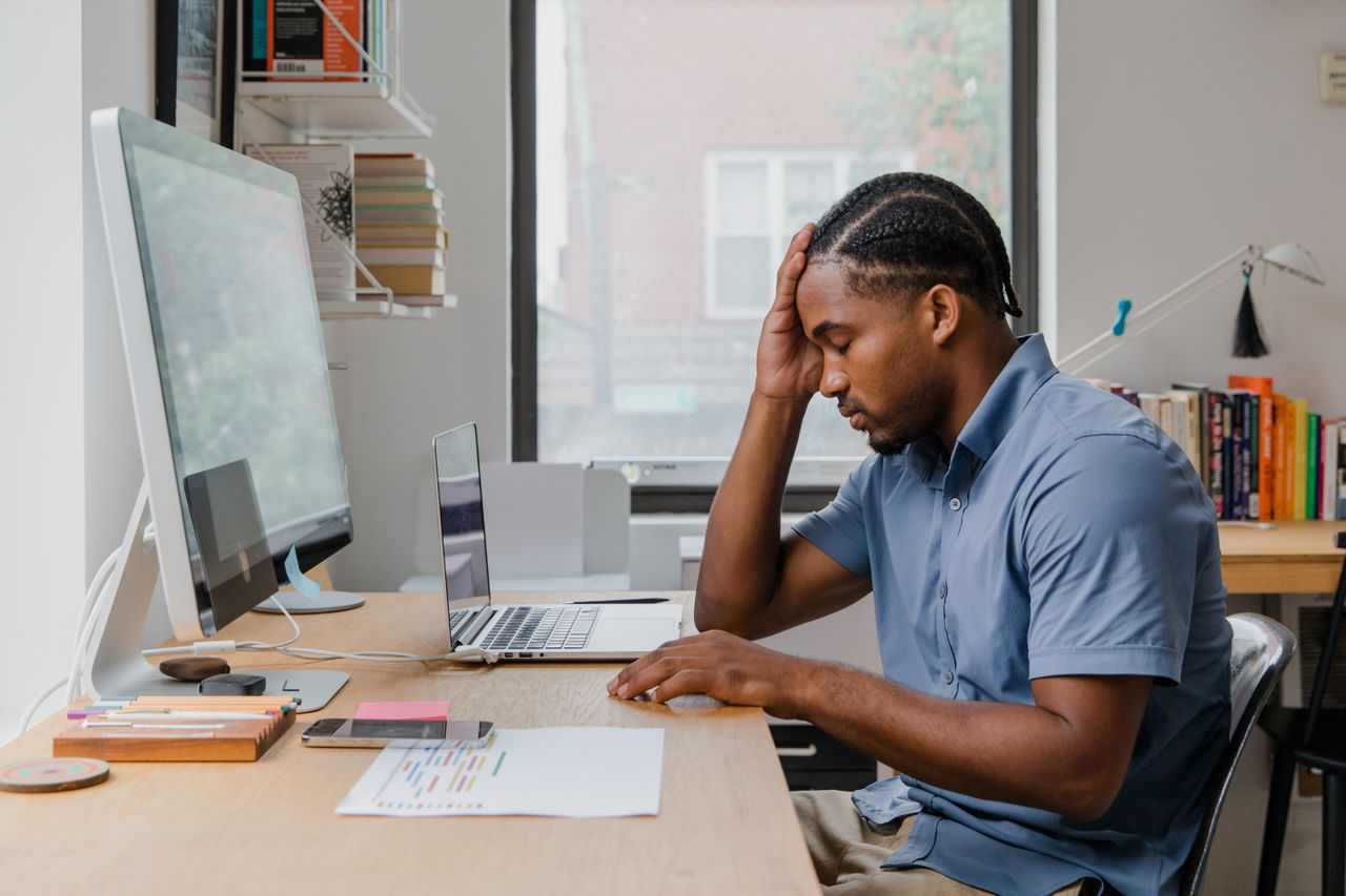 Homme débordé à son bureau, la main sur le front, devant son ordinateur