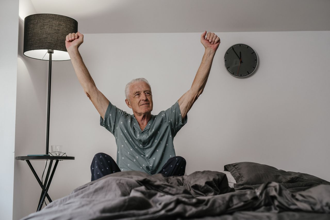 Homme âgé en pyjama qui s'étire au réveil, assis dans son lit