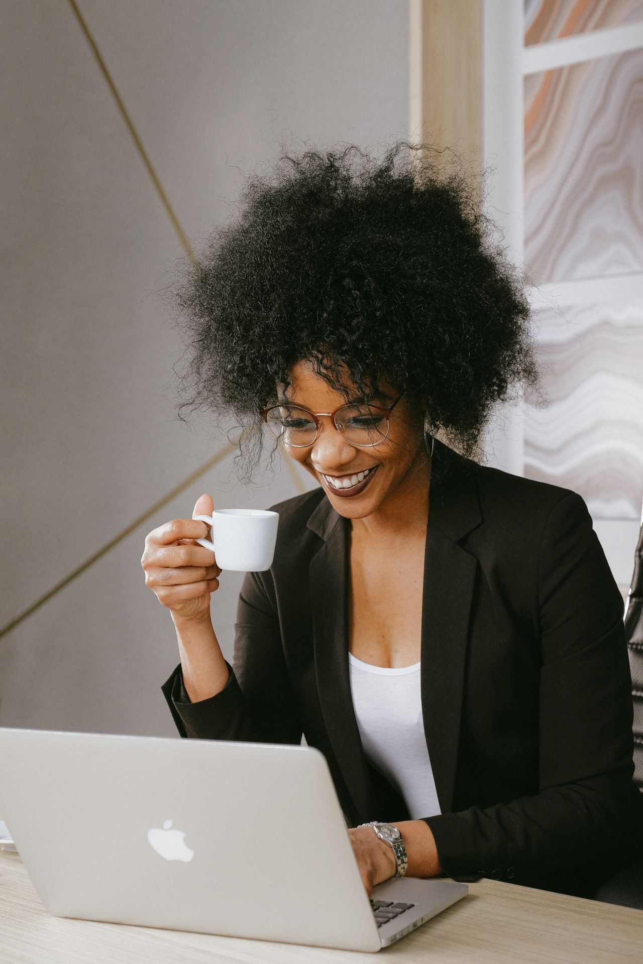 Femme souriante devant son ordinateur, une tasse de café à la main