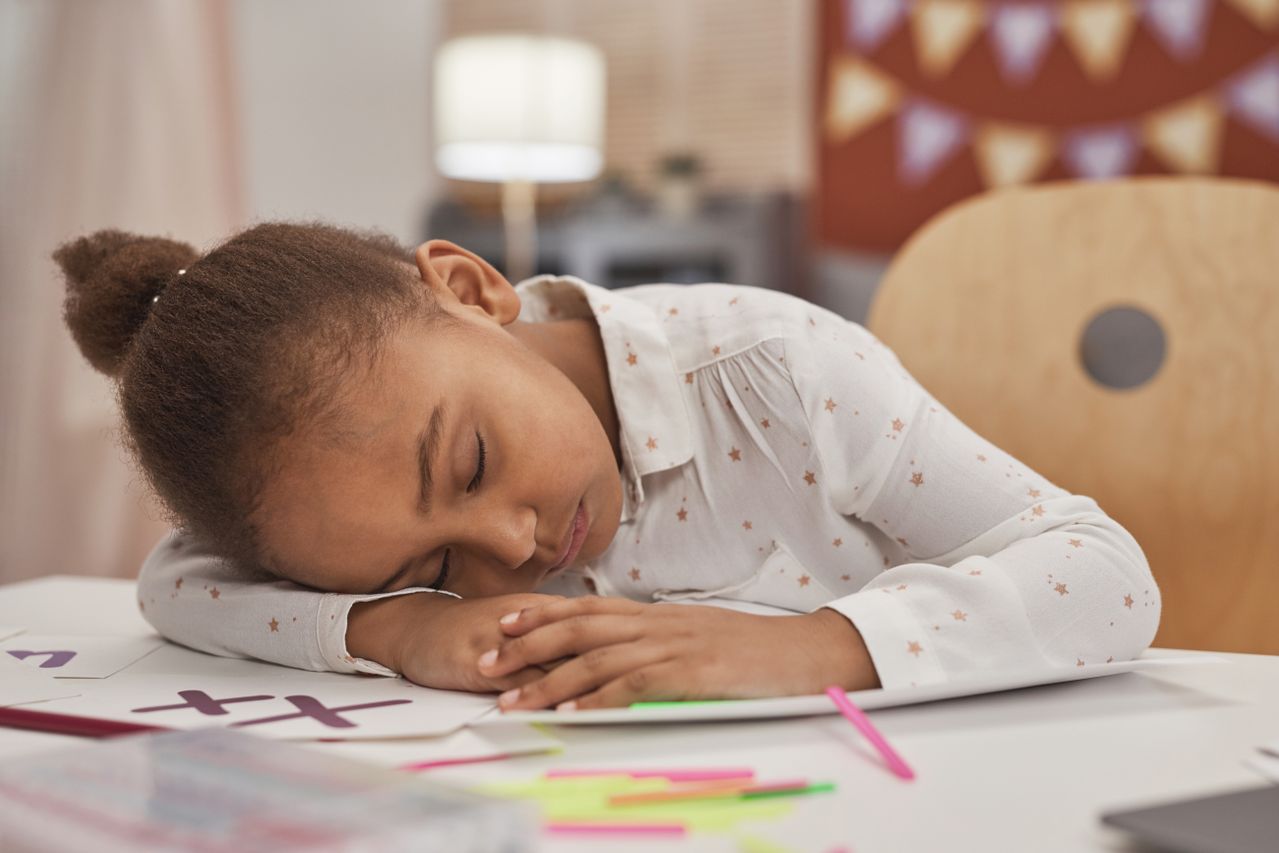 Fillette endormie sur ses devoirs, la tête posée sur les bras